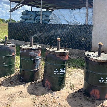 A line of steel drum kilns with chimney pipes, standing outside a covered store.